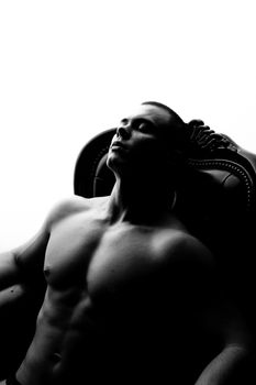 Elegant monochrome photo of a shirtless man in an armchair, capturing a serene moment.