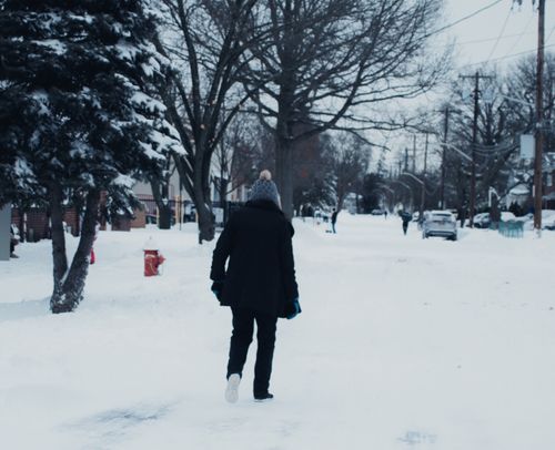 Free A person dressed warmly walks down a snowy street in winter, surrounded by trees and houses. Stock Photo