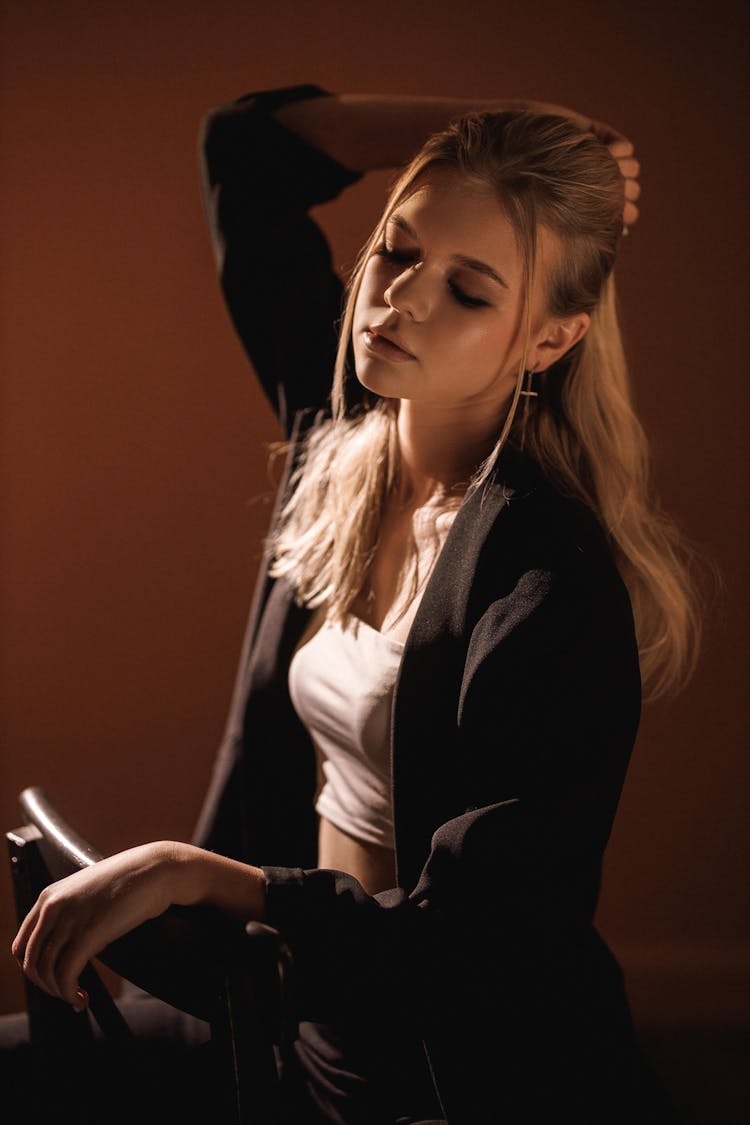 Young Blond Woman Sitting On Chair With Her Hand On Head