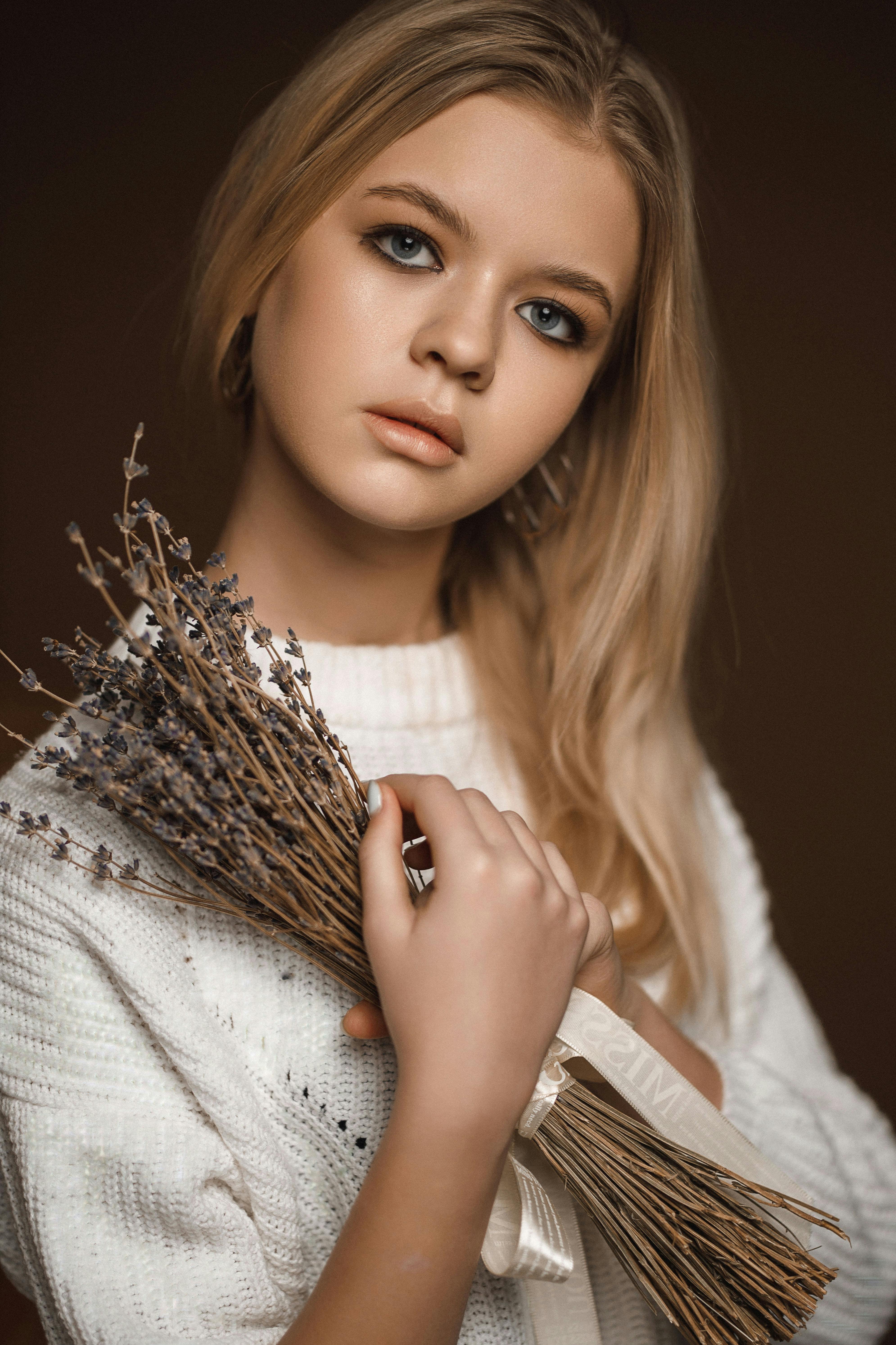 young blond woman holding bunch of dried lavender looking with tilted head