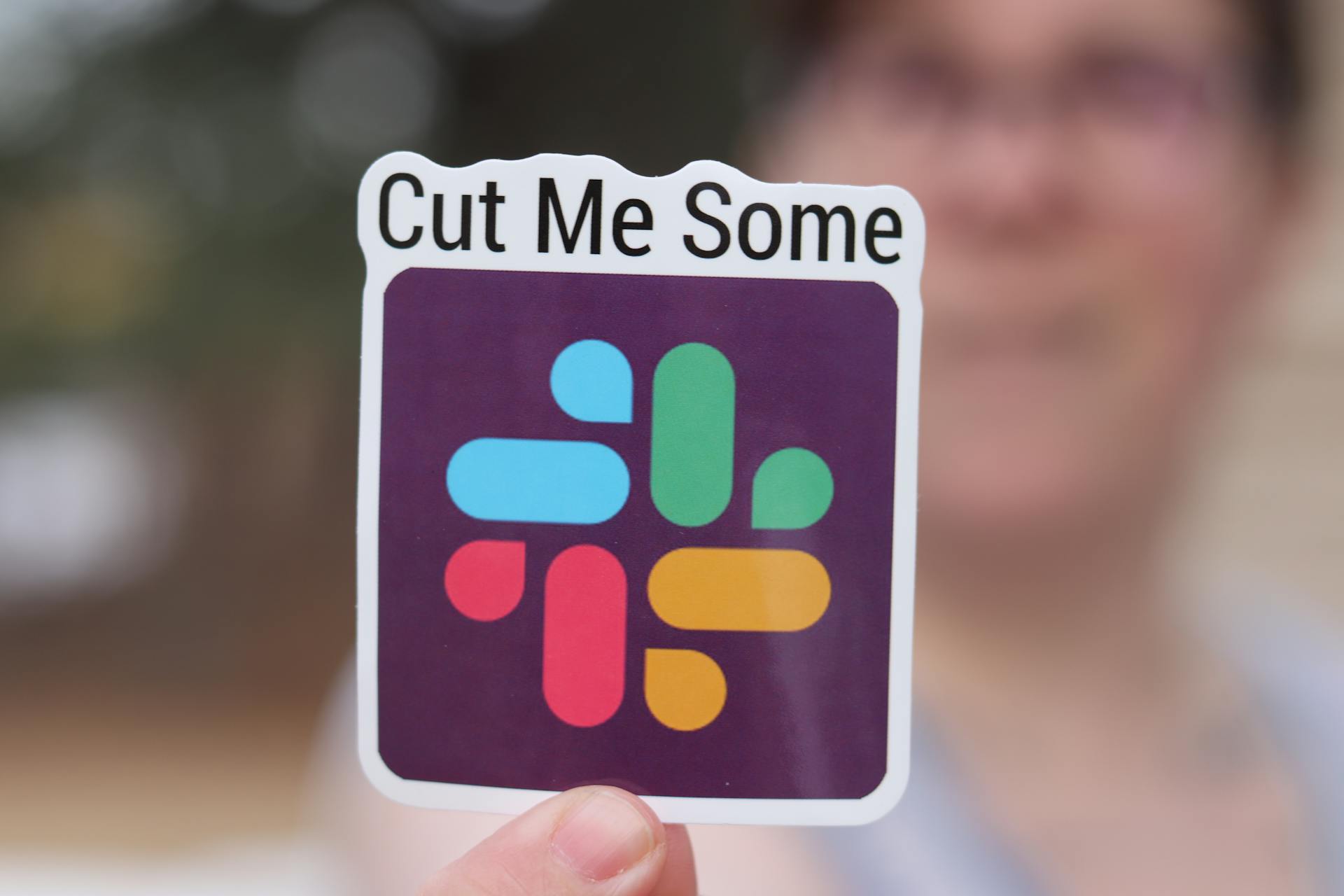 Close-up of a vibrant sticker with text 'Cut Me Some' held by a person.