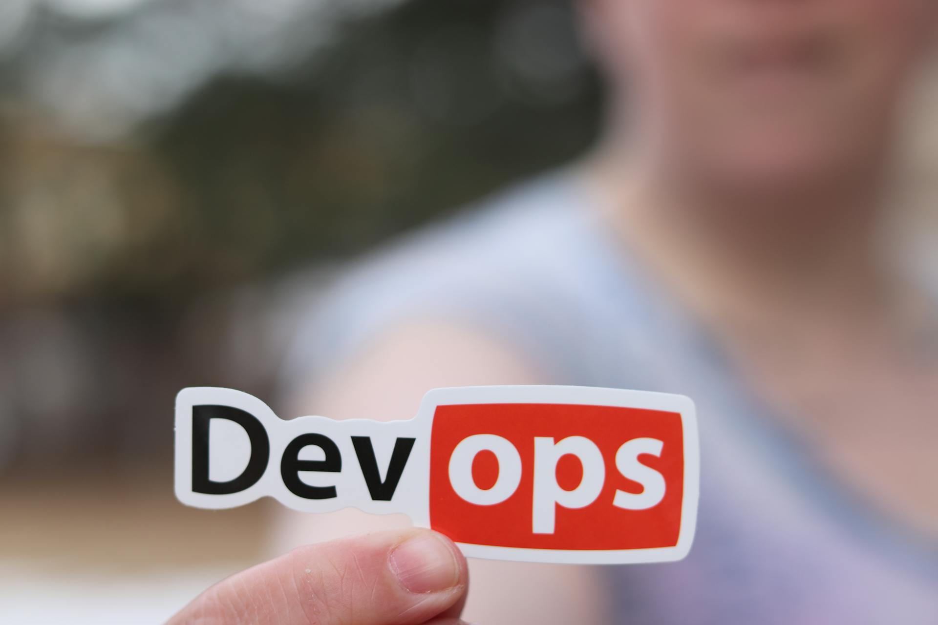 A close-up image featuring a DevOps sticker held by a person outdoors.