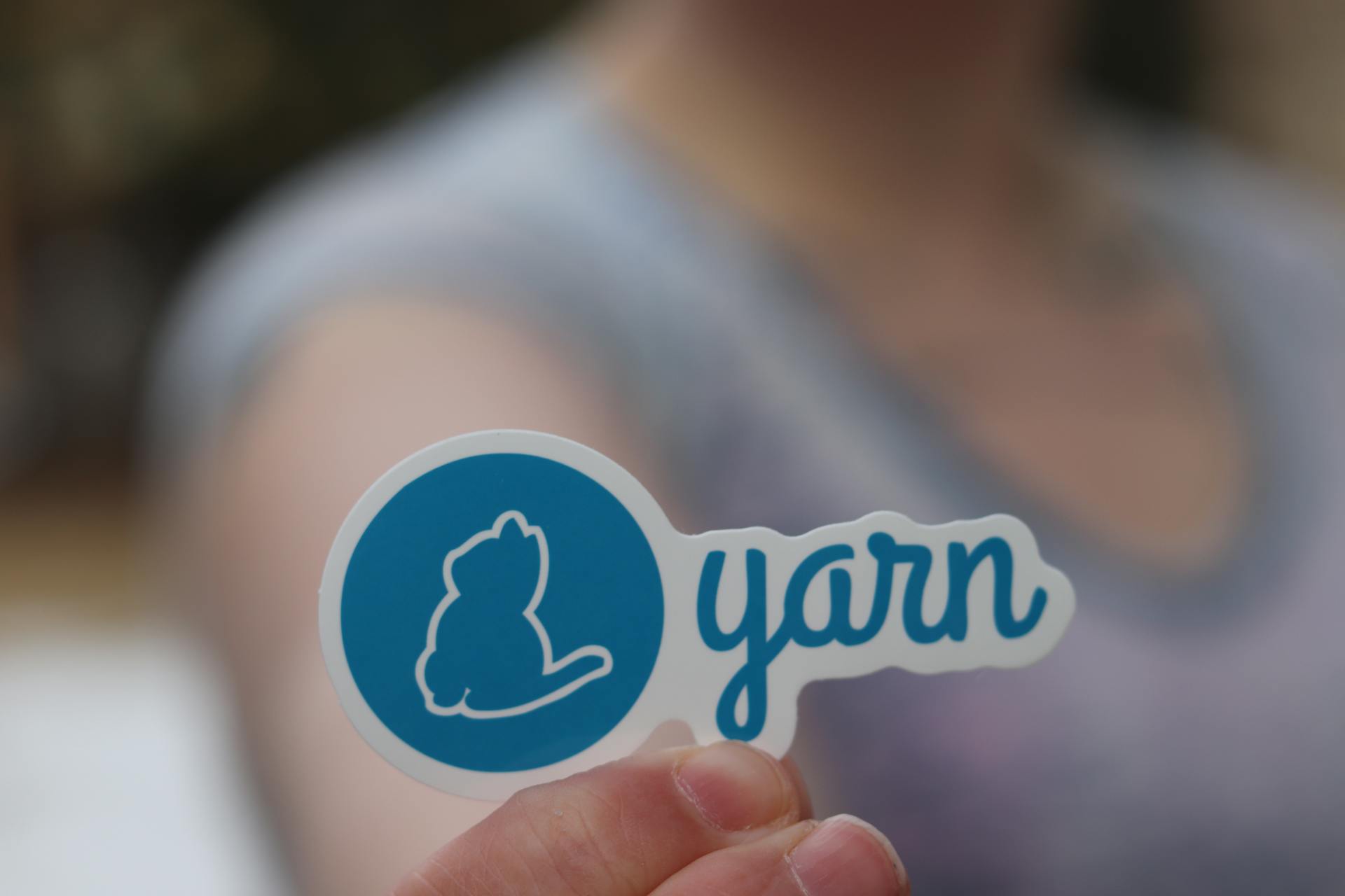 Detailed close-up of a hand holding a blue sticker featuring the Yarn logo against a blurred background.