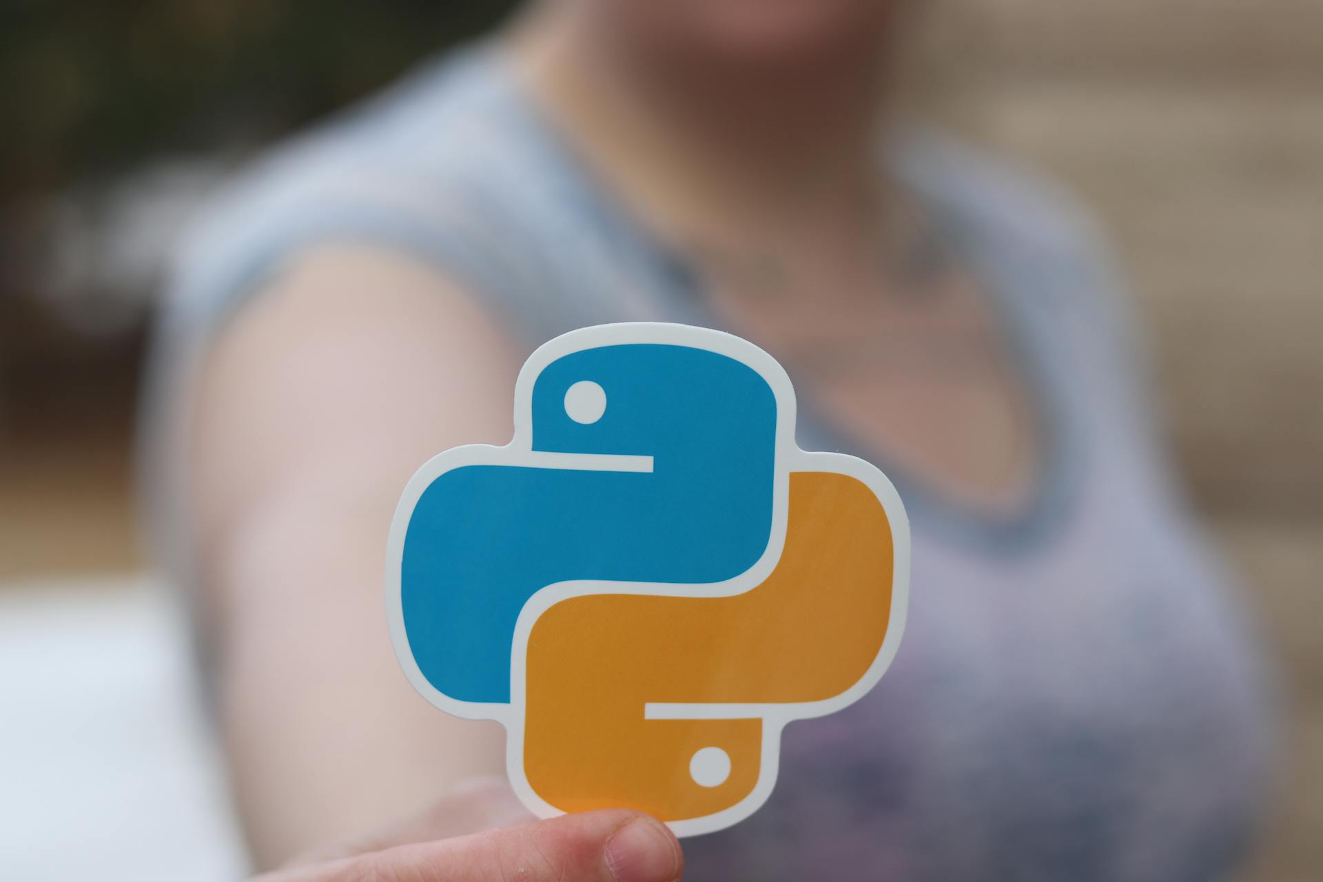 Person holding Python logo sticker with blurred background, highlighting programming focus.