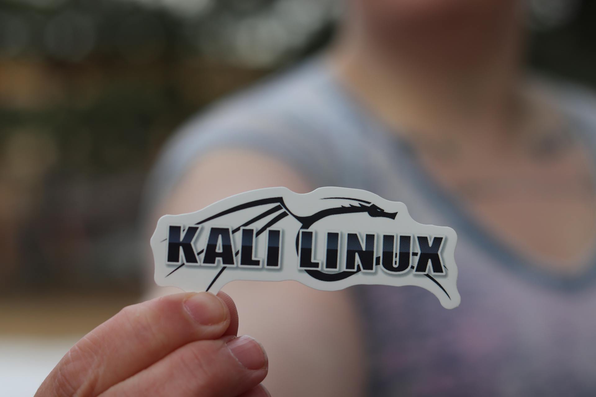 Close-up shot of a person holding a Kali Linux sticker, highlighting cyber security themes.