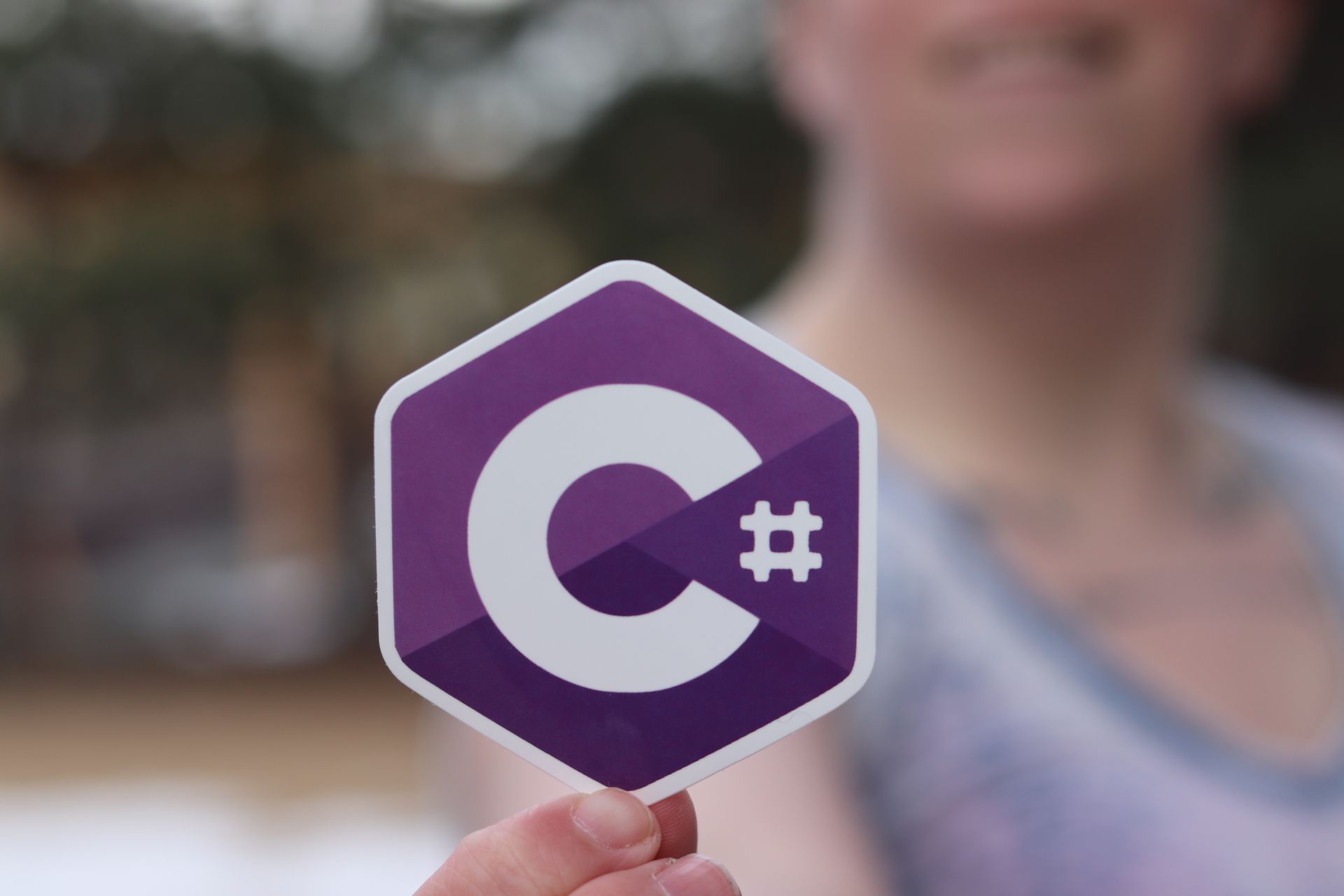 Person holding a C# programming language logo sticker outdoors.