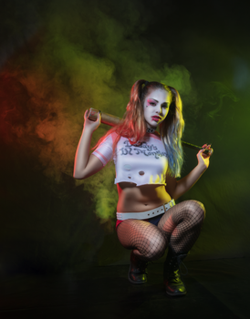 Stylized Harley Quinn cosplay photoshoot with colorful smoke effects in a dark studio setting.