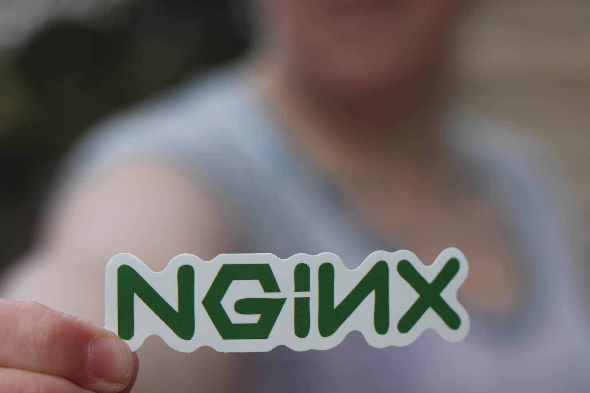 A close-up of a person holding an NGINX sticker with a blurred background.