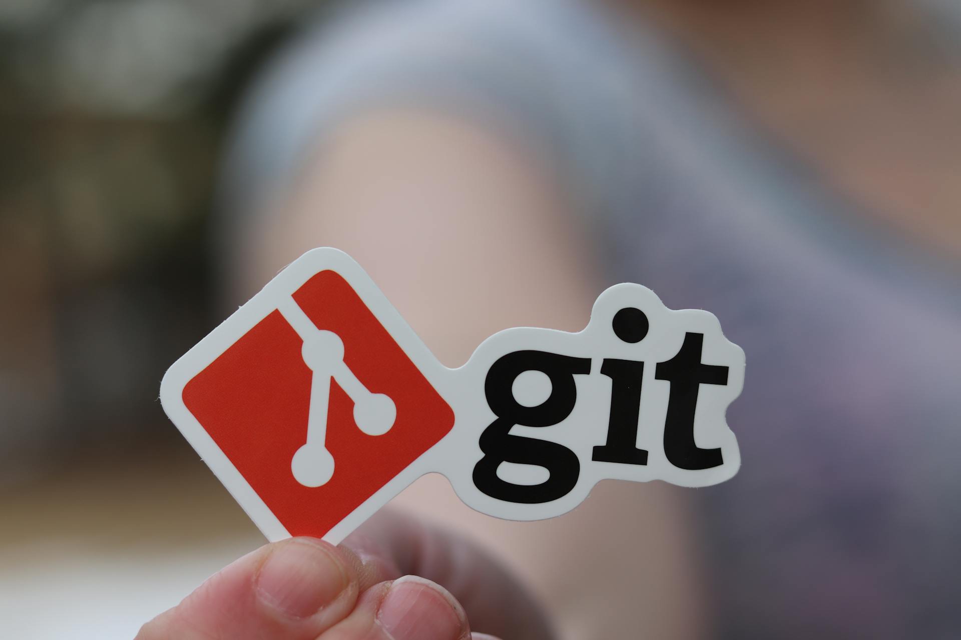 Close-up of a person holding a Git sticker, emphasizing software development.