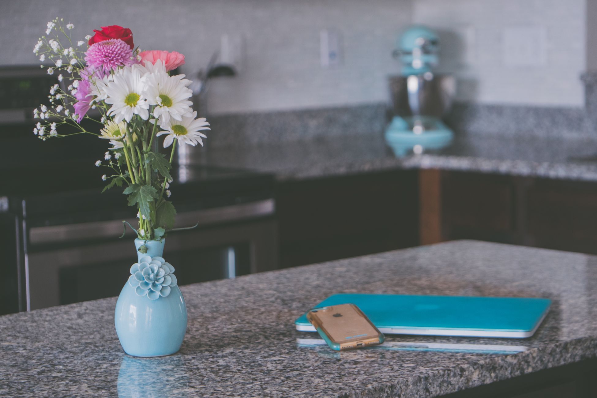 Stylish kitchen counter with floral vase, laptop, and smartphone, blending modern design.