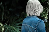 白发女子穿着牛仔夹克，被郁郁葱葱的绿色植物包围