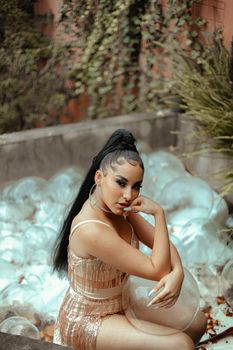 Elegant woman seated outdoors surrounded by transparent bubbles and greenery.