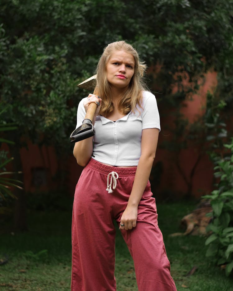 Woman Holding A Shovel On Her Shoulder And Standing In White Shirt On Garden