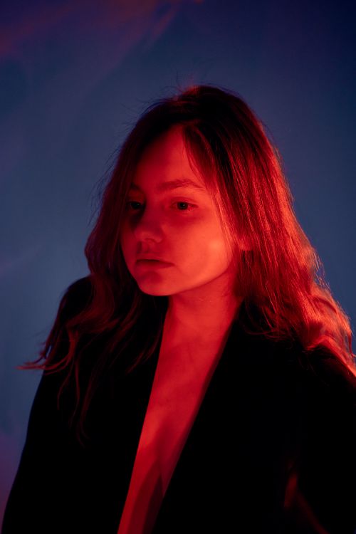 Free Portrait of a woman in a black blazer with striking red light effect against a blue background. Stock Photo