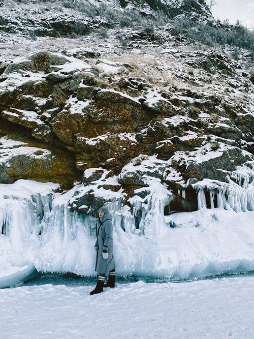 Free A woman dressed in winter clothing stands by an impressive icy rock formation, showcasing winter landscapes. Stock Photo