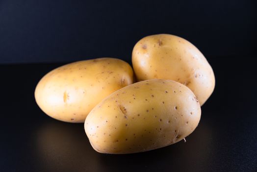 Studio shot of three fresh potatoes on a black surface, perfect for food photography.