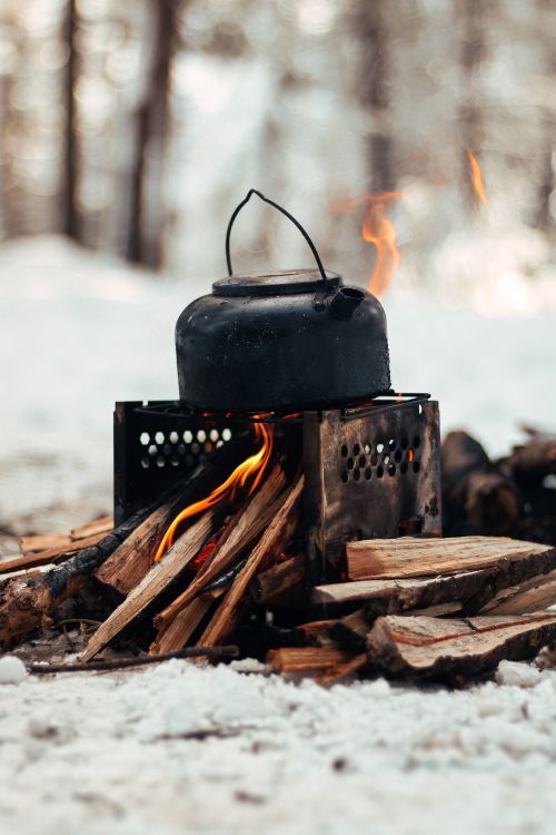 Free A kettle on a campfire brings warmth to a snowy winter forest scene. Stock Photo