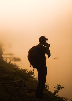 Silhouette of a lone photographer capturing a misty sunrise by a lake in Sri Lanka.