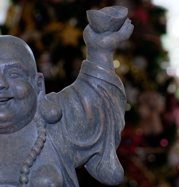 Statue de Bouddha rieur tenant un lingot d'or devant un sapin de Noël
