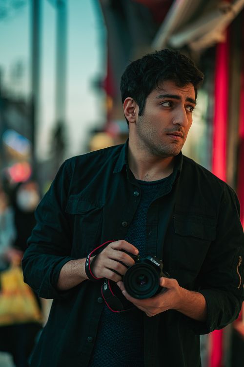 Free Man with camera in Qushchi, Iran street, capturing urban life at dusk. Stock Photo