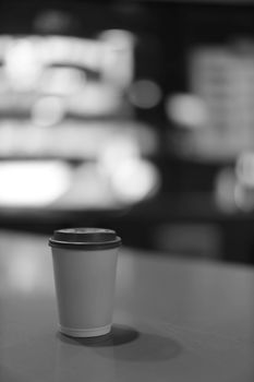 A grayscale image of a paper cup on a table in a café, highlighting minimalist design.