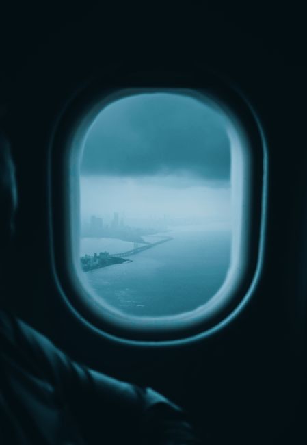 Dramatic view of a city's skyline through a plane window with moody, dark tones.