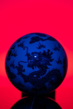 Close-up of a blue ceramic ball with dragon pattern on a vivid red background.