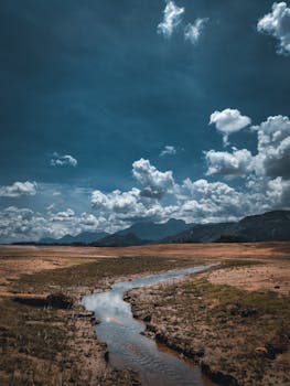 Breathtaking view of a serene valley with a winding river and majestic mountains under a dramatic cloudy sky.