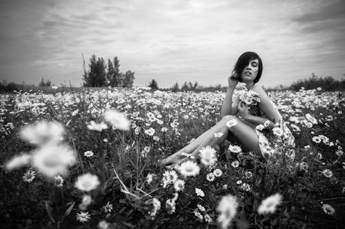 Grayscale Photo of Woman Sitting Beside Daisies