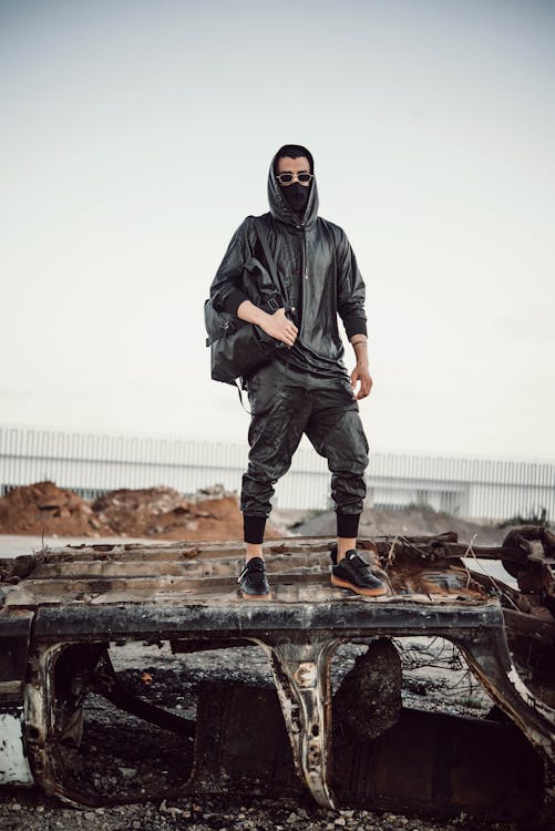 A Man in Black Hoodie Jacket Standing on Top of a Decayed Vehicle