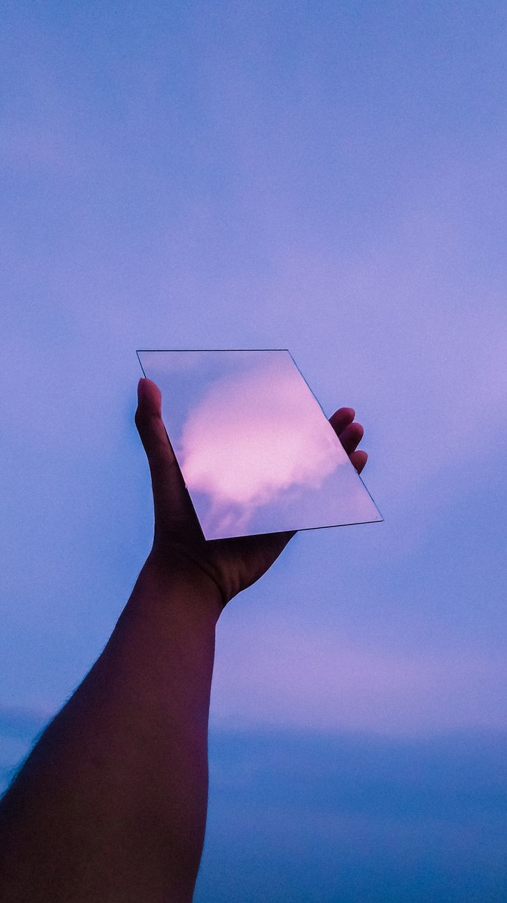A hand holding a mirror reflecting a colorful sunset sky creating a surreal effect.