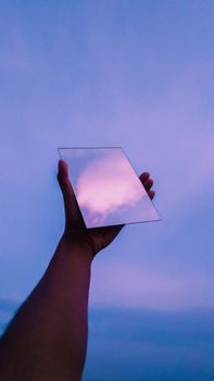 A hand holding a mirror reflecting a colorful sunset sky creating a surreal effect.