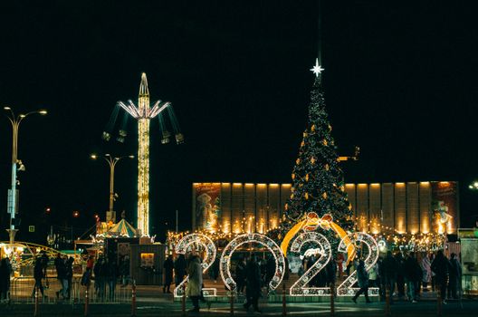 Festive night at an illuminated Christmas carnival with a giant tree and 2022 lights.
