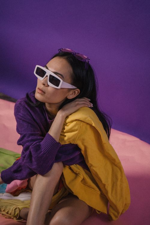 Free Fashionable woman in colorful attire and sunglasses seated against a vibrant background. Stock Photo