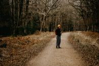 Boy in Black Jacket Walking on Pathway Between Trees