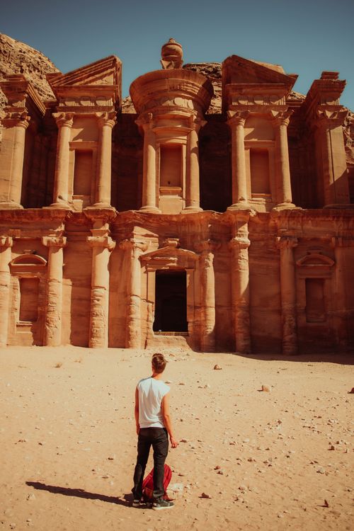 Free Back view of a traveler standing in front of the iconic Petra Monastery in Jordan's desert landscape. Stock Photo