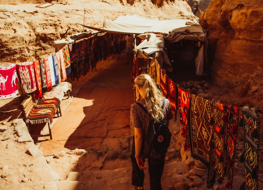 Woman browsing colorful textiles in a market passage in Wadi Musa, Jordan.