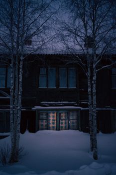 A cozy wooden house with lit windows on a snowy winter night. Serene and mysterious.