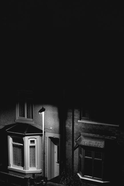 A dark minimalist view of UK housing under streetlight illumination, conveying solitude at night.