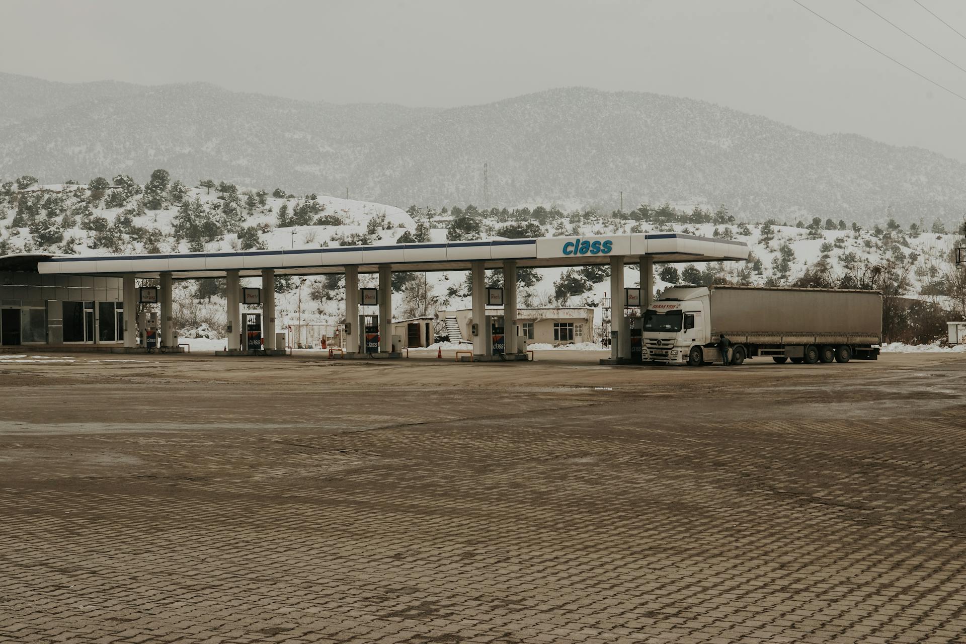A snowy gas station with a truck and mountains in the backdrop, offering a serene winter scene.