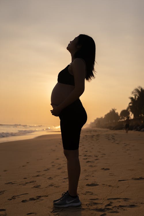 Free Side View of a Pregnant Woman Standing on the Sand Stock Photo