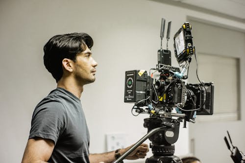 A Side View of a Man in Gray Shirt Using a Camera Equipment