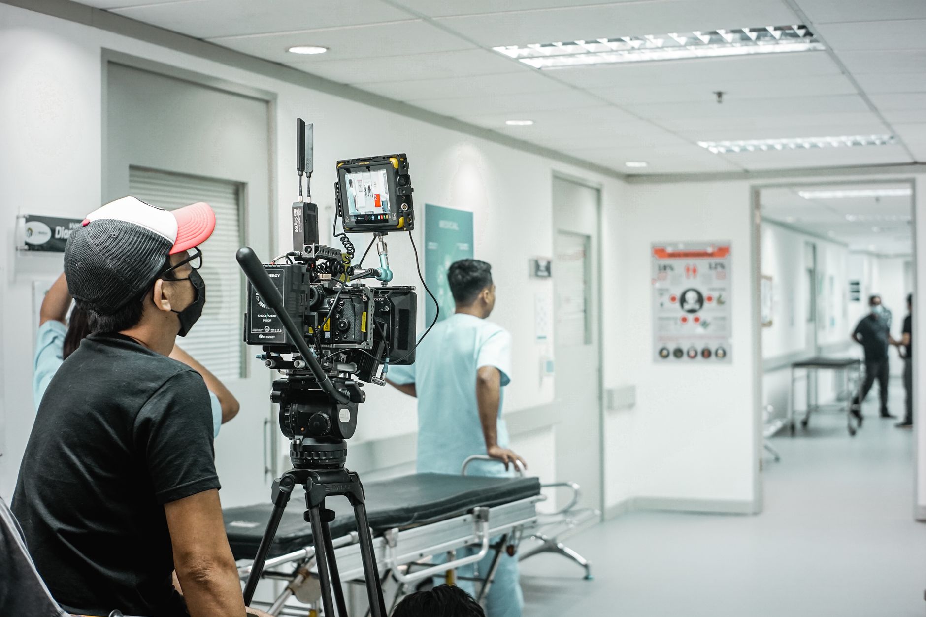 Cameraman capturing a scene in a hospital corridor with a professional video camera.
