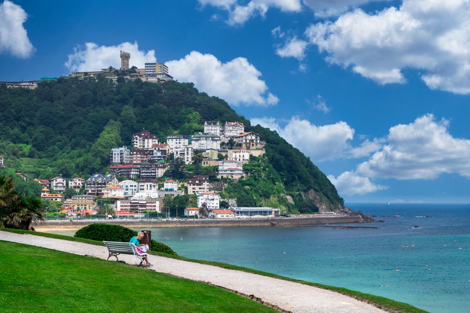 Picturesque view of a coastal town with hillside houses and a peaceful oceanfront path.
