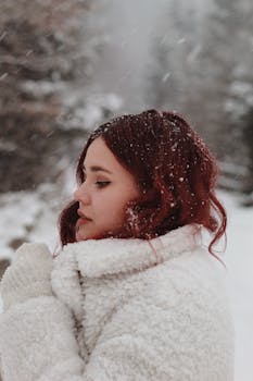 Side profile of a woman in a fur coat standing outdoors in a snow-covered landscape during winter.