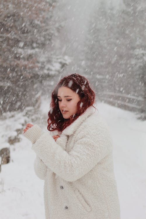 A Woman in White Winter Coat Standing Outside while Snowing