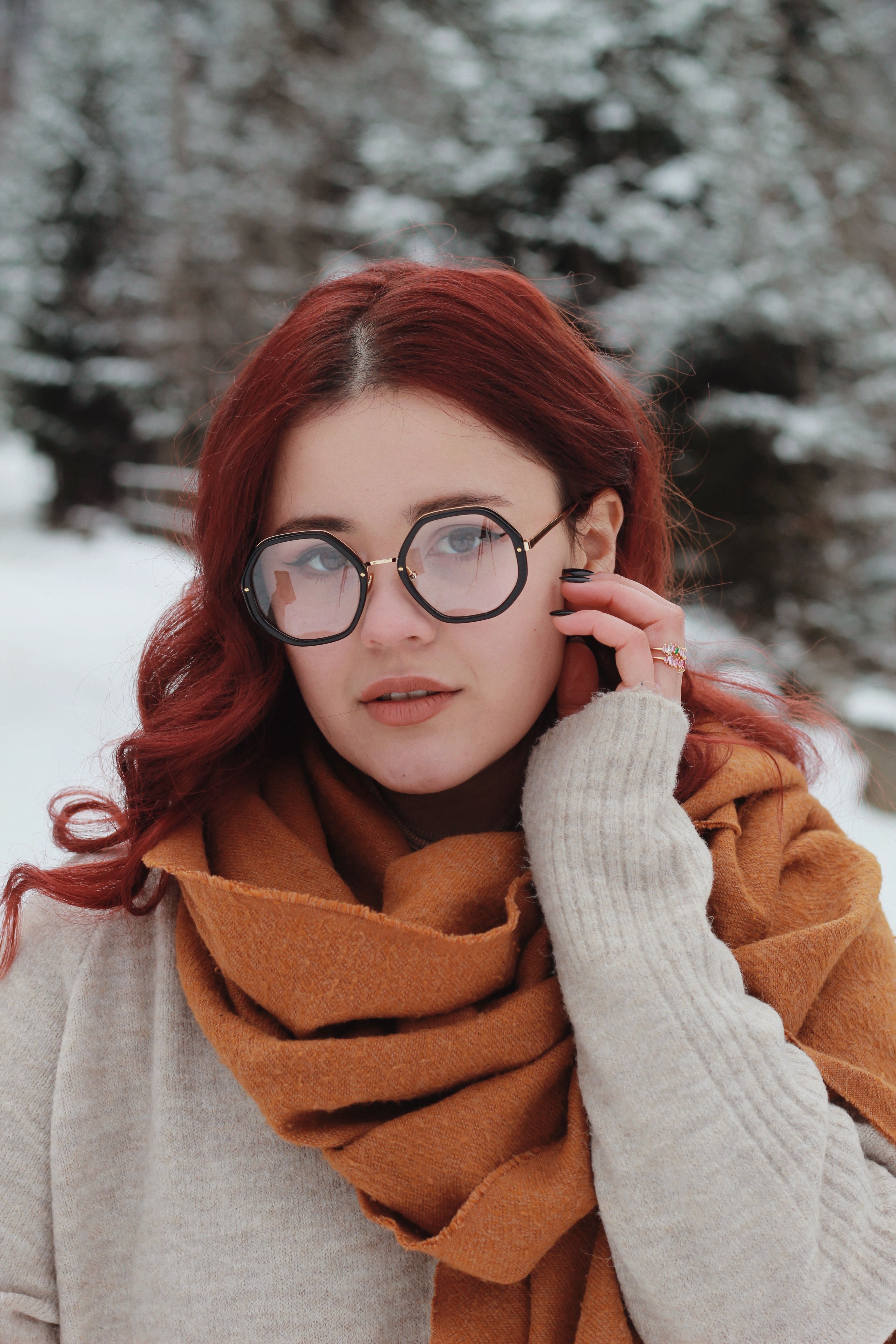 Young woman with red hair and glasses in a snowy forest. Winter fashion portrait highlighting warm tones and serene expression.