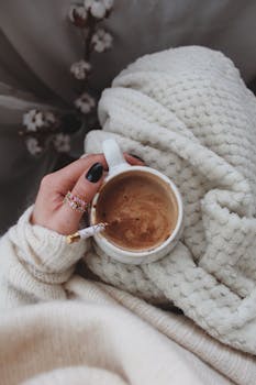 Warm coffee held in a hand wrapped in a knitted sweater, evoking coziness.