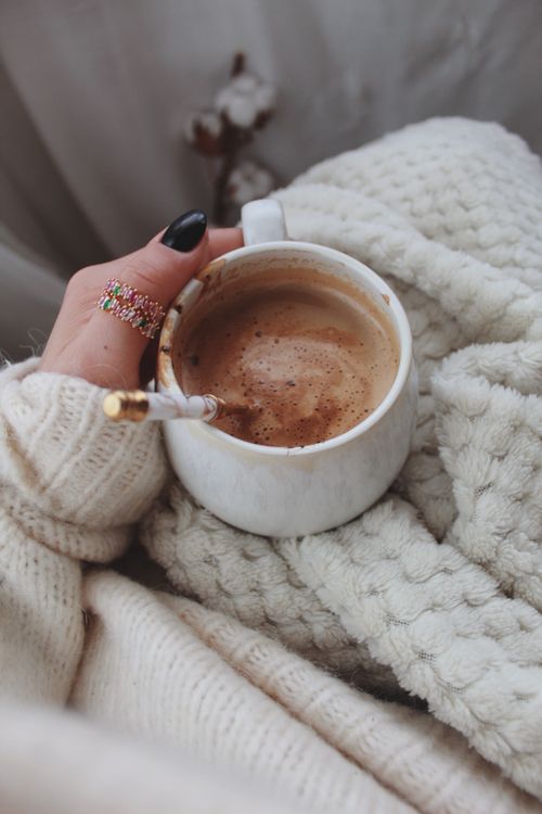 Free Close-up of a hand holding a coffee mug, wrapped in a cozy sweater and blanket. Stock Photo