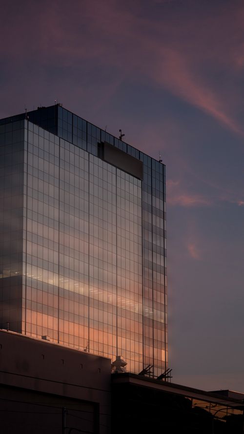 Free A modern skyscraper with reflective glass windows at dusk, capturing the city's skyline. Stock Photo